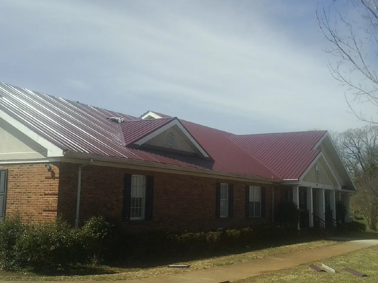 Red metal roof with gabled entries on a long brick building, from a Hail Damage Roof Repair job in Leslie