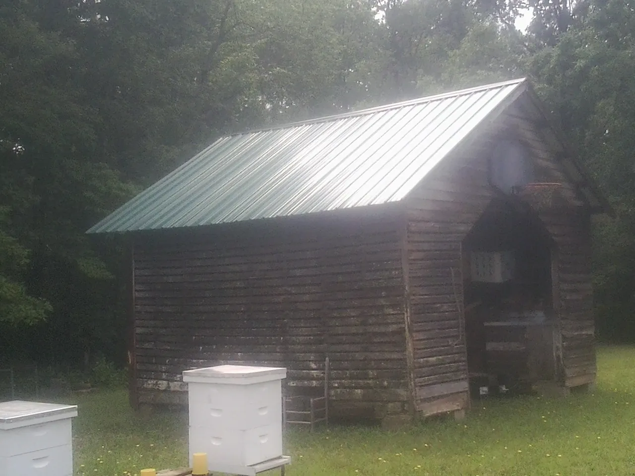 Green metal roof on a weathered barn beside stacked beehives in Leslie