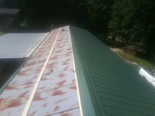 Old rusted panels beside newly installed green metal roofing — Wind Damage Roof Repair by Roofing Brothers in Leslie