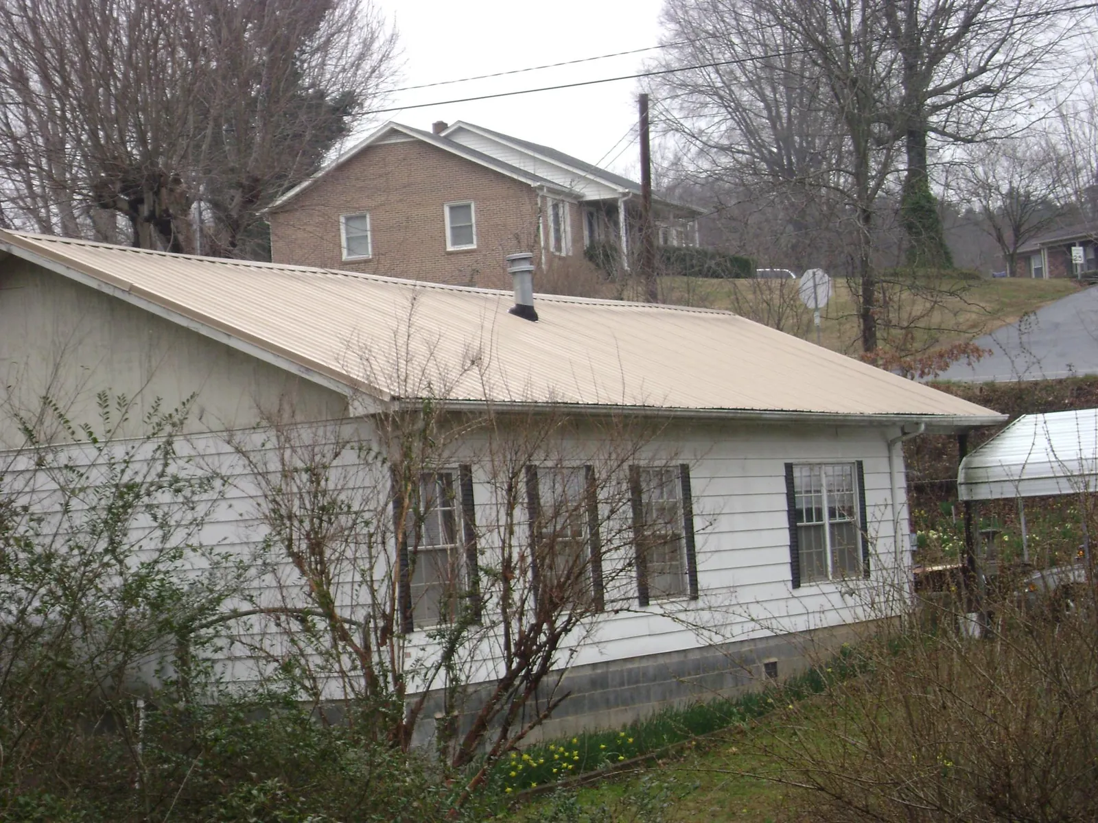 Tan metal roof on a white sided house set into a hillside — Commercial Roofing by Roofing Brothers in Leslie