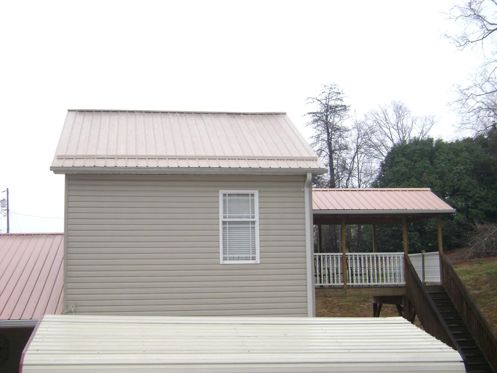 Tan metal roofs on a two story addition and attached porch, from a Roof Replacement job in Leslie